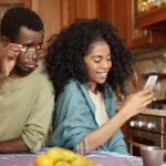 jealous-curious-black-man-holding-glasses-spying-his-girlfriend-s-mobile-phone-while-she-is-typing-message-her-lover-smiling-happily-betrayal-unfaithfulness-infidelity-lack-trust